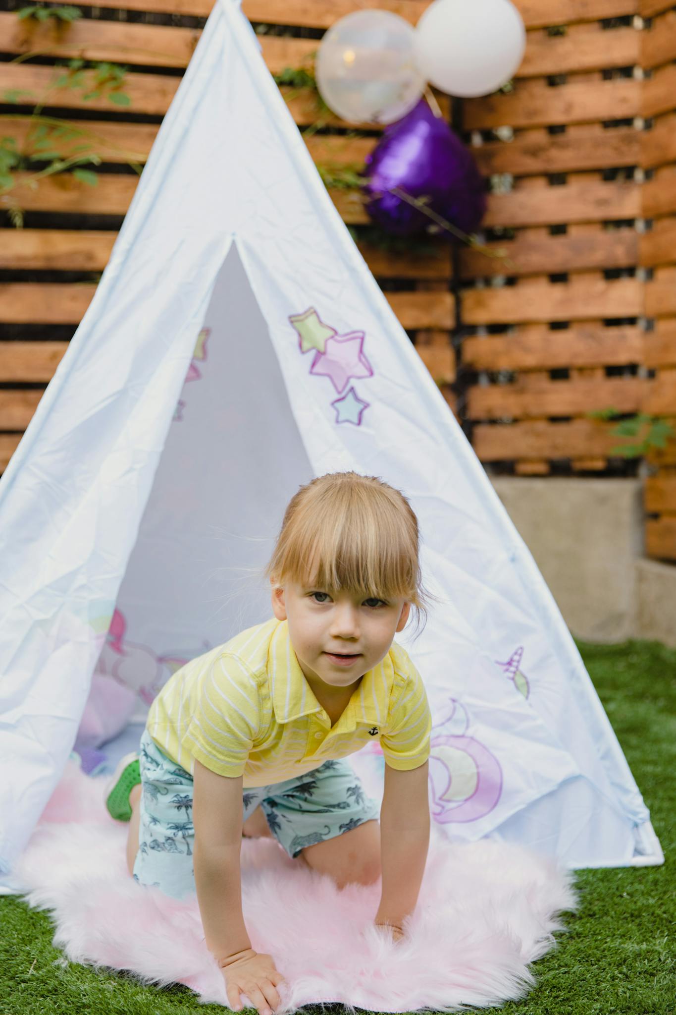 A young child enjoying playtime in a garden with a teepee tent and balloons.