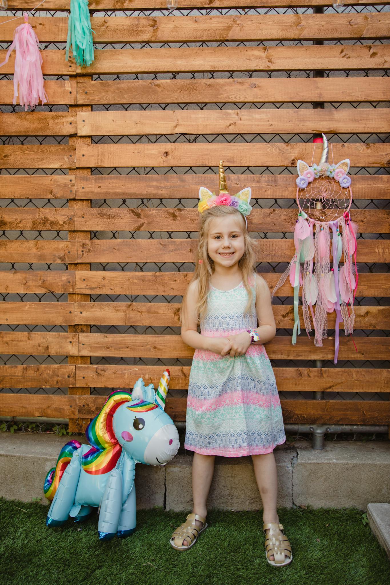 Adorable girl celebrating birthday outdoors with unicorn decorations, showcasing happiness and fun.