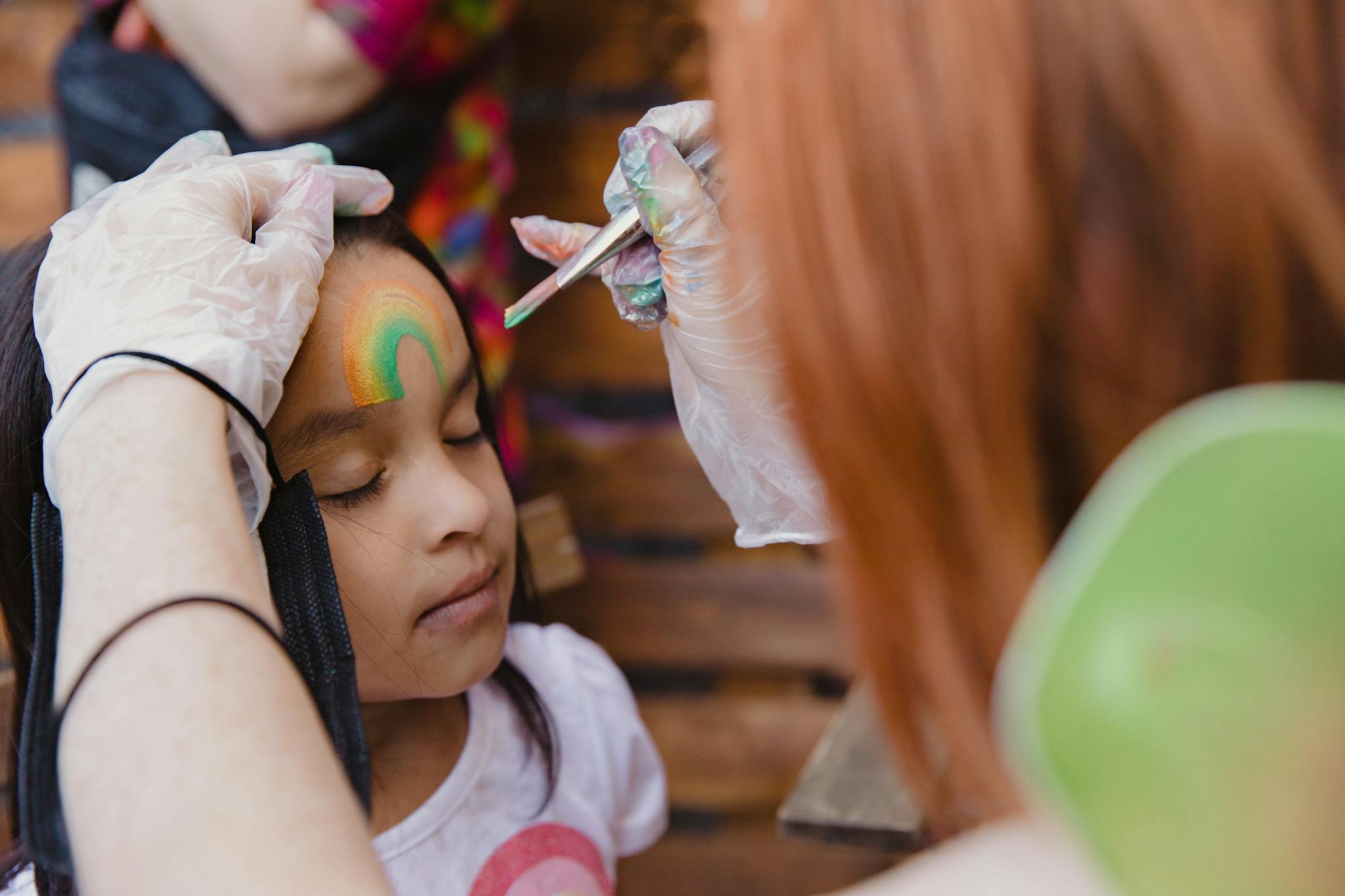 Close-up of a young girl getting her face painted at a lively children's party.