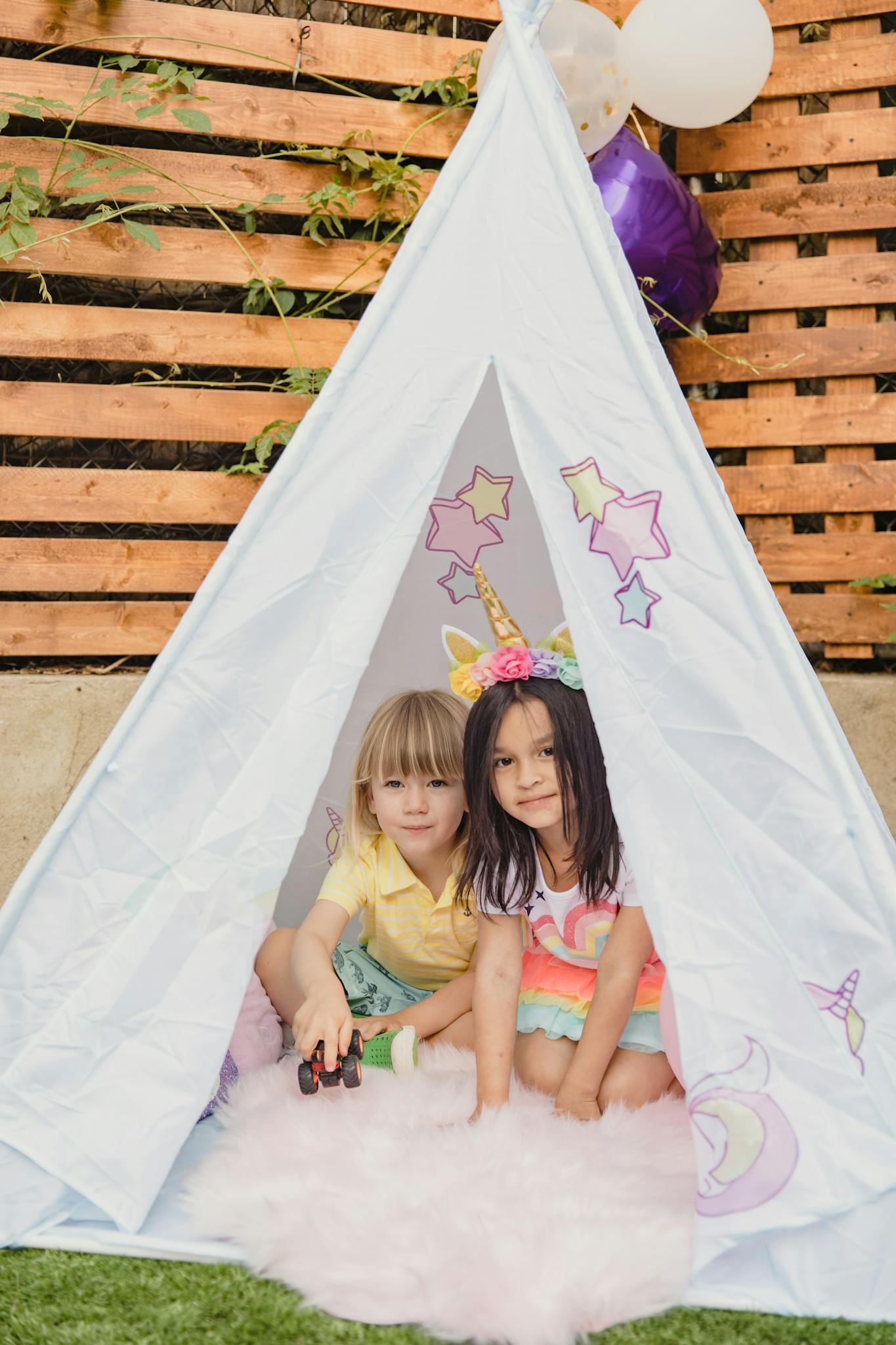 Two children enjoying a playful moment inside a colorful tent at a festive outdoor party.
