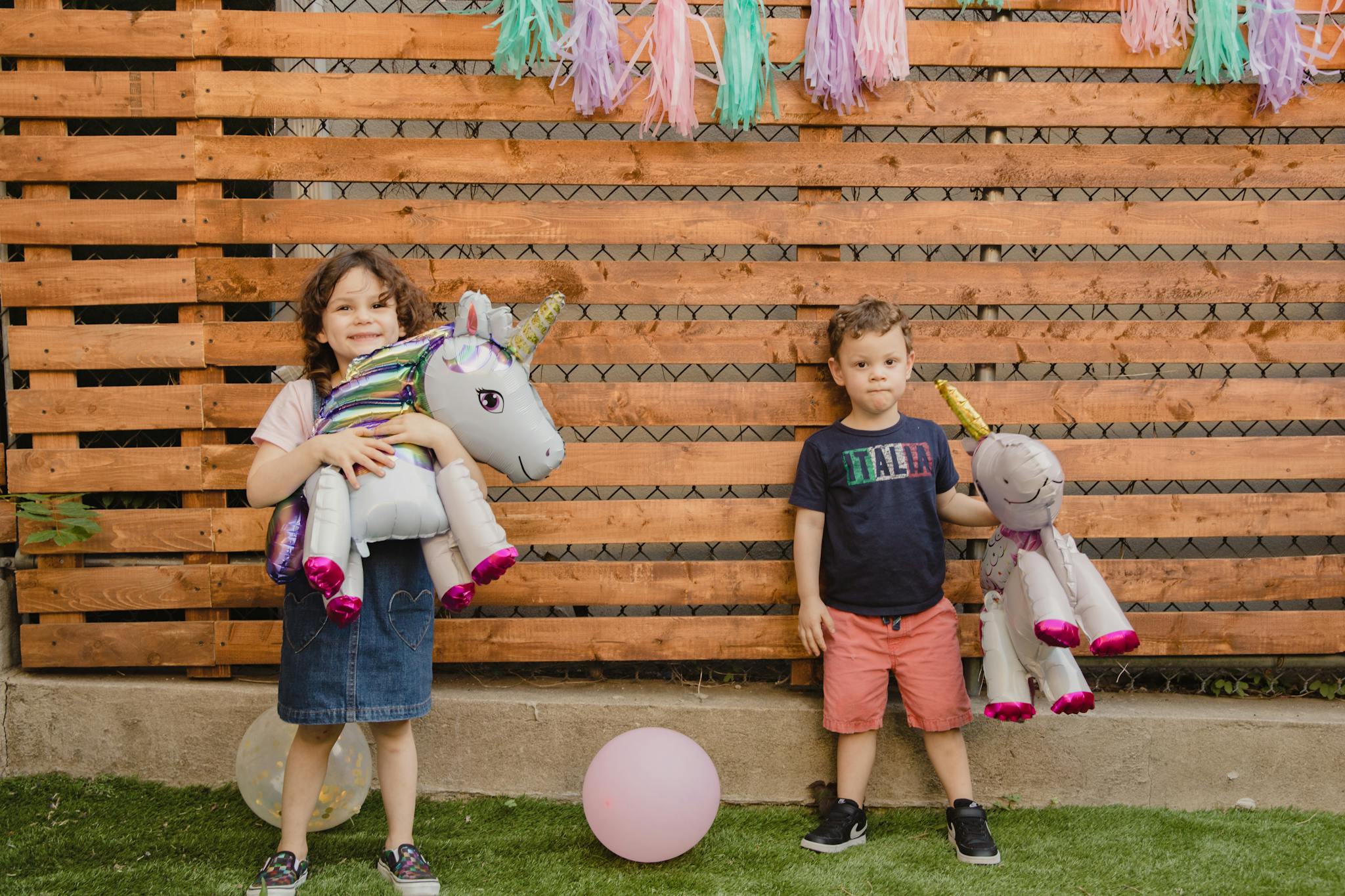 Two children holding unicorn balloons at an outdoor party with decorations.
